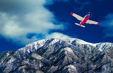 single engine aircraft flying over snow capped peaks.