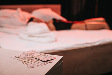 selective focus of dollar banknotes on bedside table near woman on bed