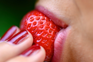 A ripe strawberry freshly picked, from which a young woman is about to bite off.