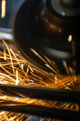 Worker cutting, grinding and polishing motorcycle metal part with sparks indoor workshop. Super macro close-up. Vertical