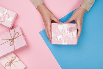 Womans hands holding gift or present box on pink pastel table top view. Flat lay  for birthday or New Year.
