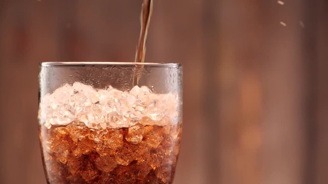 Cola pouring in tall glass with ice cubes in slow motion. A lot of bubbles and sparkling.