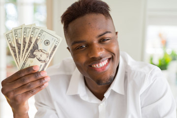 African american man holding twenty dollars bank notes with a happy face standing and smiling with...