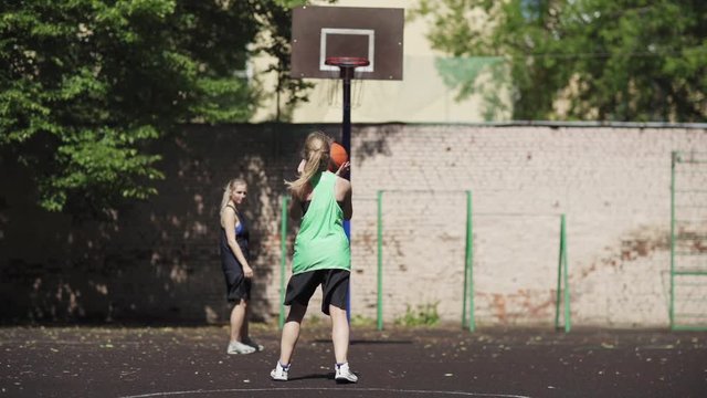 Two athletic college girls practicing basketball shots on street court. Female basketball player shooting hoop and scoring goal in slow motion