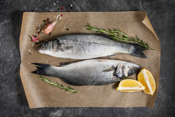 Fresh fish seabass and ingredients for cooking, lemon and rosemary. Dark background top view.