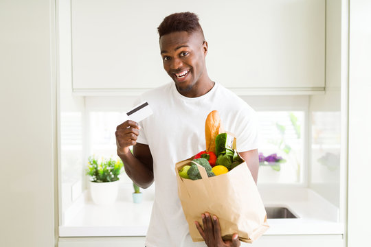 African american man holding paper bag full of groceries and holding credit card as payment