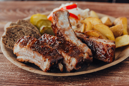Delicious beef ribs with sauce, fried potatoes, cucumber, cabbage and khlobe in a paper plate on a wooden table. takeaway street food
