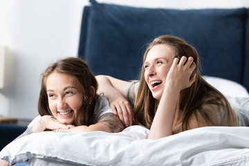 two laughing lesbians lying on bed in morning in bedroom
