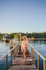 Fototapeta premium Vacation on tropical island. Young woman in hat enjoying sunset sea view from wooden bridge terrace, Siargao Philippines.