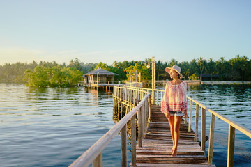 Vacation on tropical island. Young woman in hat enjoying sunset sea view from wooden bridge terrace, Siargao Philippines.