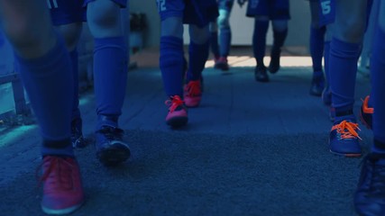 Low section shot of soccer players in uniform and boots going one by one from crosswalk to grass and starting to run