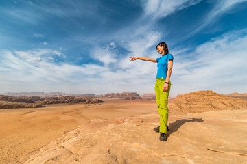 Fototapeta na wymiar Young girl above desert pointing to red sand dunes with nice blue sky above, Wadi Rum, Jordan