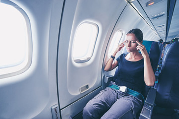 Fear of flying woman in plane airsick with stress headache and motion sickness or airsickness. Person in airplane with aerophobia scared of flying being afraid while sitting in airplane seat.