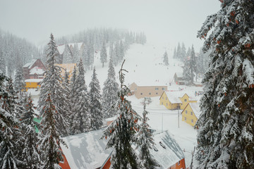 Beautiful white winter wonderland mountain scenery in the Carpathian with traditional houses. Skiers and snowboarders skiing downhill to village.