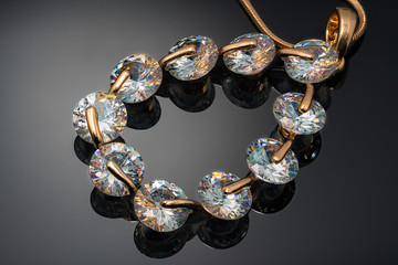jewel, yellow metal pendant with precious stones on dark background with reflection