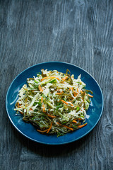 Salad of white cabbage, sea kale and fresh carrots seasoned with olive oil, dill and parsley. Dark wooden background.