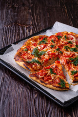 Freshly cooked hot pizza and slice with cheese ham meat tomato onion parsley homemade on parchment paper in baking sheet tray recipe on dark wooden table