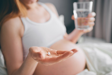 Medicine and pragnancy. Young pregnant woman holding pill and glass of water in her hand.