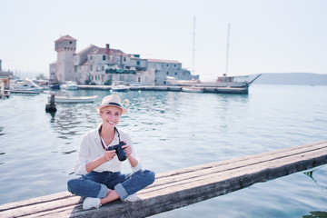Fototapeta na wymiar Tourism concept. Young traveling woman enjoying the view of Kastel Gomilica Castle sitting near the sea on Croatian coast.