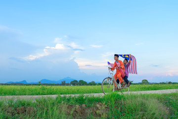 independence Day concept - Two happy young local boy riding old bicycle at paddy field holding a Malaysian flag