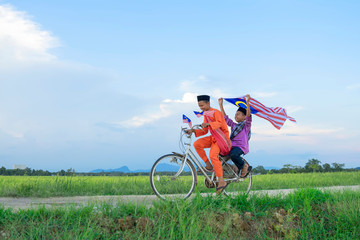 Fototapeta premium independence Day concept - Two happy young local boy riding old bicycle at paddy field holding a Malaysian flag