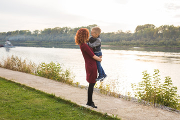 Motherhood and children concept - young mother with son in her arms near the river