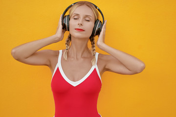 Summer vacation. Studio portrait of happy young woman with earphones enjoying sounds of music. Yellow background.