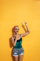 Your text here. I have an idea!Amazed beautiful young woman pointing up while standing against yellow wall.