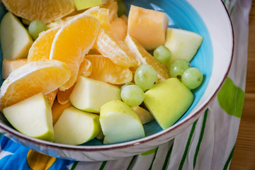 Naklejka na ściany i meble A bowl of fresh fruit, apples, grapes, melon and orange on a wooden table. Shallow depth of focus.