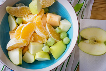 A bowl of fresh fruit, apples, grapes, melon and orange on a wooden table. Shallow depth of focus.