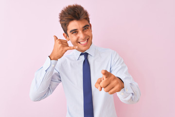 Young handsome businessman wearing shirt and tie standing over isolated pink background smiling doing talking on the telephone gesture and pointing to you. Call me.
