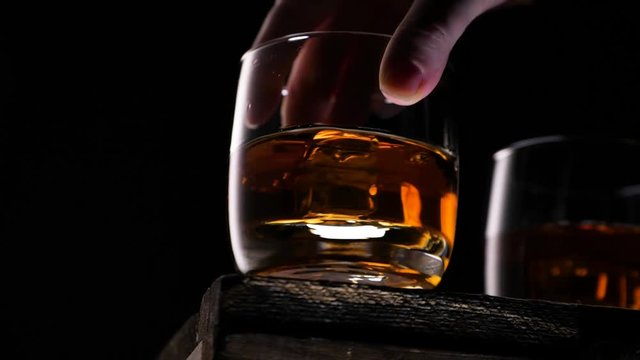 Someone puts the glass with golden whiskey on the table. Only hand in the frame. Slow motion.