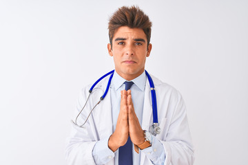 Young handsome doctor man wearing stethoscope over isolated white background begging and praying with hands together with hope expression on face very emotional and worried. Asking for forgiveness. 