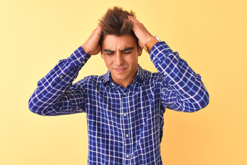 Young handsome man wearing casual shirt standing over isolated yellow background suffering from headache desperate and stressed because pain and migraine. Hands on head.