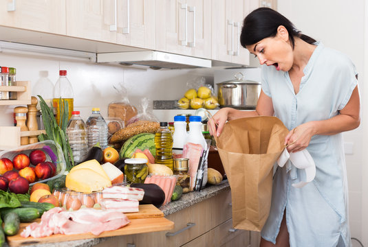 Woman is standing with paper bag and is sading because forgot to buy ingridient for recipe at home.
