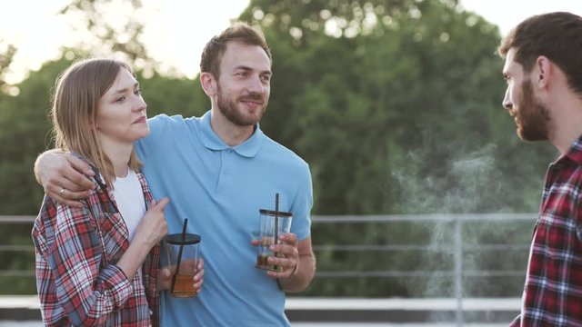 Happy young friends cooking barbecue food at the party outdoors. Grop portrait of a couple and man smiling talking together telling stories outdoors in the city.