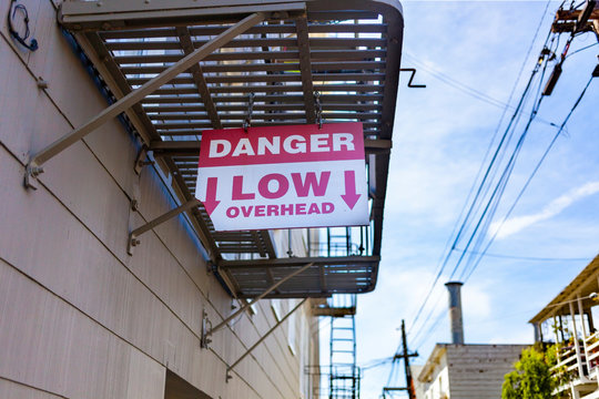 OSHA Compliant DANGER LOW OVERHEAD Sign Hanging From Urban Building Fire Escape.