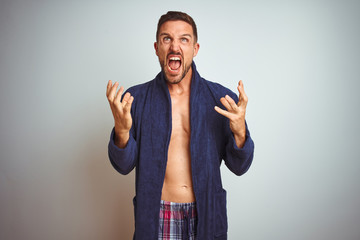 Fototapeta premium Sexy shirtless man wearing comfortable pajamas and robe over isolated background crazy and mad shouting and yelling with aggressive expression and arms raised. Frustration concept.