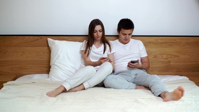 Guy shows his girlfriend photo on his phone. Girl laughs. Young couple watching photos on mobile phone in modern white interior. Beautiful young of couple of man and woman is using smartphone at home