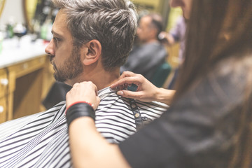 Hipster client covered with cape waiting for haircut.