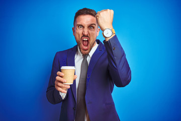 Young handsome business man drinking a coffee on a paper cup over blue isolated background annoyed and frustrated shouting with anger, crazy and yelling with raised hand, anger concept