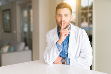 Young handsome doctor man at the clinic asking to be quiet with finger on lips. Silence and secret concept.