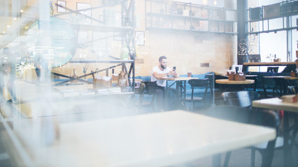 Man using a tablet pc at a restaurant or coffee place. He is wearing white t-shirt and sitting by a table