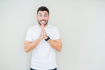 Young handsome man wearing casual white t-shirt over isolated background praying with hands together asking for forgiveness smiling confident.