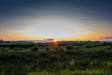Fototapeta na wymiar Yellow-orange disk of the setting sun over the horizon and a little cloudy.