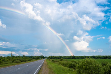 Multicolor rainbow against a cloudy sky and a wet asphalt road.