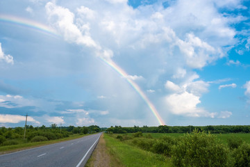Multicolor rainbow against a cloudy sky and a wet asphalt road.