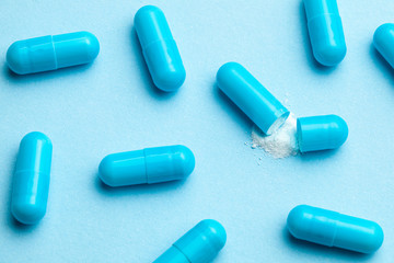 Blue tablets in capsules. One capsule is open. Blue background