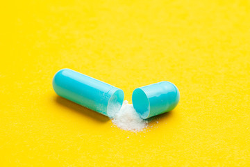 Blue tablets in capsules. One capsule is open. Yellow background.