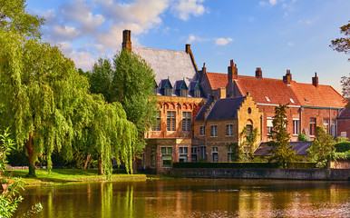 Obraz premium Vintage building over lake of love in Minnewater park in Bruges Belgium near Beguinage monastery of Beguines. Picturesque landscape with green trees sunset time.